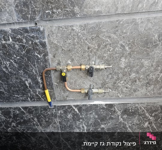 צינור גז עם ברזים ומחברים על קיר שיש אפור